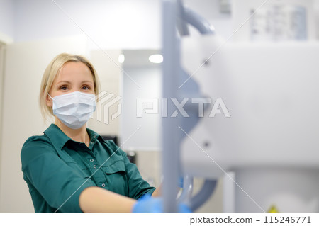Female technician adjusts X-Ray machine. Female radiologist is going to take an Xray of patient in X-ray room of modern clinic. Female technician adjusts X-Ray machine. Female radiologist is going to take an Xray of patient in X-ray room of modern clinic. 115246771
