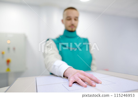 Young man having x-ray shot of broken hand in x-ray room in modern clinic. Patient wearing in protect lead apron 115246953