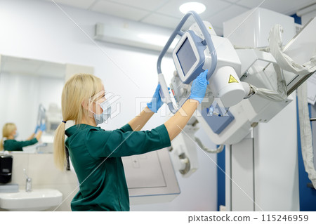 Female technician adjusts X-Ray machine. Female radiologist is going to take an Xray of patient in X-ray room of modern clinic. 115246959
