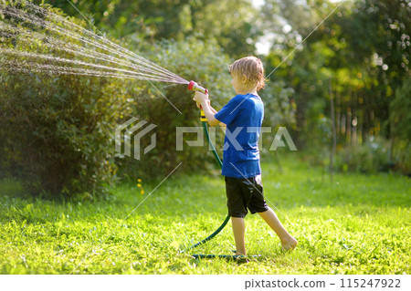 Funny little boy playing with garden hose in sunny backyard. Preschooler child having fun with spray of water. Summer vacation in the village for kids. Funny little boy playing with garden hose in sunny backyard. Preschooler child having fun with spray of water. Summer vacation in the village for kids. 115247922