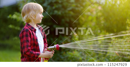 Cute boy watering plants and playing with garden hose with sprinkler in sunny backyard. Preschooler child having fun with spray of water. Summer outdoors activity for kids. Gardening. Banner. 115247929