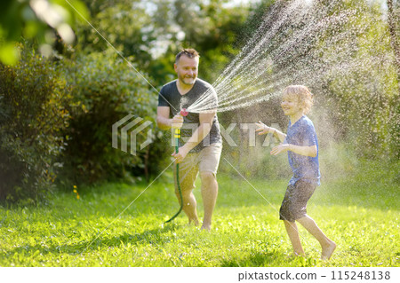 Funny little boy with his father playing with garden hose in sunny backyard. Preschooler child having fun with spray of water. Summer outdoors activity for kids. Funny little boy with his father playing with garden hose in sunny backyard. Preschooler child having fun with spray of water. Summer outdoors activity for kids. 115248138