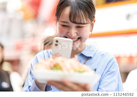 A young, cute, SNS-loving woman taking a photo of takoyaki with her smartphone outdoors in bright light | Dotonbori Shopping Street, Osaka City, Osaka Prefecture A young, cute, SNS-loving woman taking a photo of takoyaki with her smartphone outdoors in bright light | Dotonbori Shopping Street, Osaka City, Osaka Prefecture 115248592