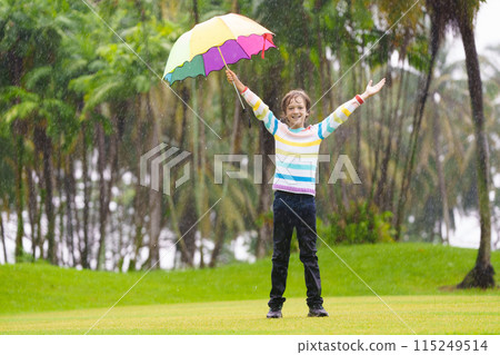 Child playing in rain. Kid jumping in puddle. 115249514