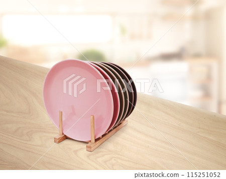 Ceramic plates in a wooden stand on a wooden table There is a blurred image of the kitchen in the background. Ceramic plates in a wooden stand on a wooden table There is a blurred image of the kitchen in the background. 115251052