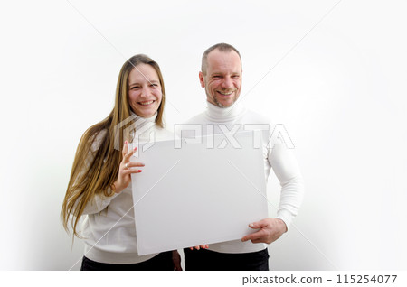 adult man and a young woman holding a picture in their hands a frame for advertising text smiling sincere laughter white clothes white background place empty frame paper cardboard poster banner adult man and a young woman holding a picture in their hands a frame for advertising text smiling sincere laughter white clothes white background place empty frame paper cardboard poster banner 115254077