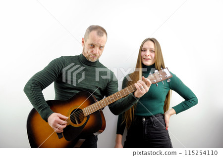 curly man sitting on couch and playing acoustic guitar near happy woman with teddy bear curly man sitting on couch and playing acoustic guitar near happy woman with teddy bear 115254110