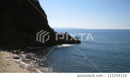 Clear blue skies, blue ocean, and a sandy beach lined with strangely shaped rocks 115254116