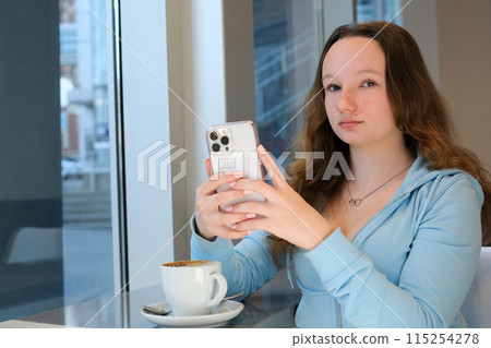Girl texting on the smart phone in a restaurant terrace with an unfocused background Girl texting on the smart phone in a restaurant terrace with an unfocused background 115254278