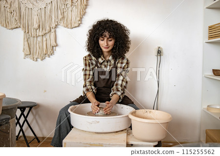 Female potter crafting ceramic bowl at pottery wheel in studio 115255562
