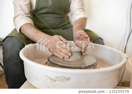 Male potter sculpting clay bowl using pottery wheel in studio Male potter sculpting clay bowl using pottery wheel in studio 115255579