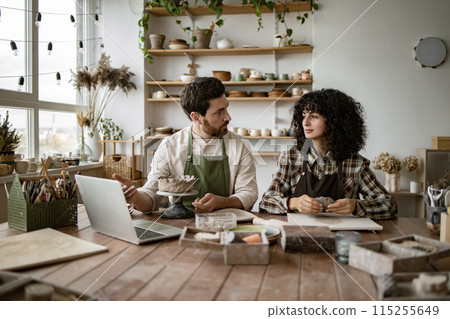 Mature man and young woman sculpting clay in pottery workshop 115255649