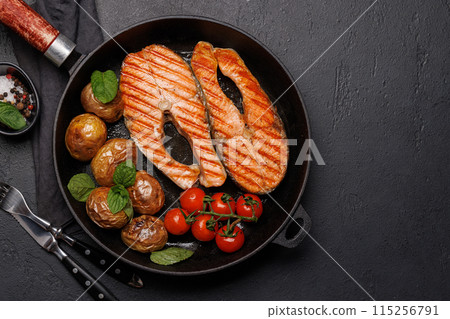 Grilled salmon steaks and potatoes sizzling in a frying pan 115256791