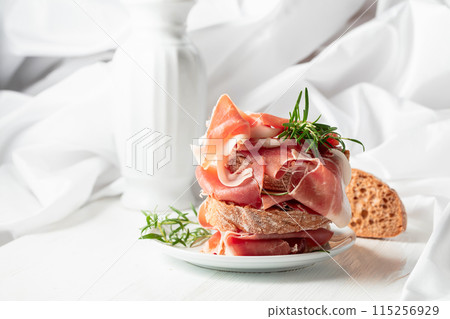 Ciabatta with prosciutto and rosemary on a white wooden table. Ciabatta with prosciutto and rosemary on a white wooden table. 115256929