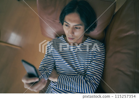 Young man using smartphone on sofa Young man using smartphone on sofa 115257354