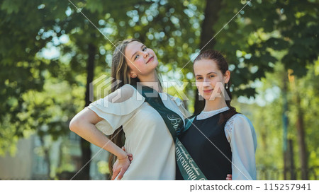 Two Russian schoolgirls graduate posing on a summer day. Two Russian schoolgirls graduate posing on a summer day. 115257941