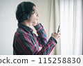 A young man listening to music on a smartphone 115258830