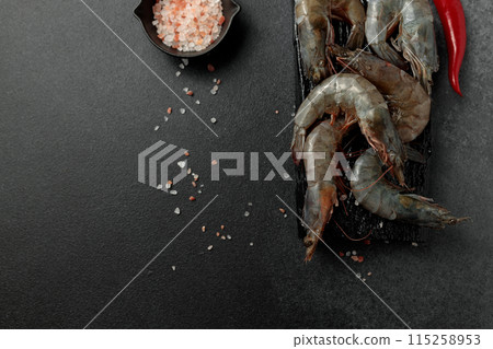 Large king prawns raw on a black cutting board. Hot pepper, salt. Black background Large king prawns raw on a black cutting board. Hot pepper, salt. Black background 115258953