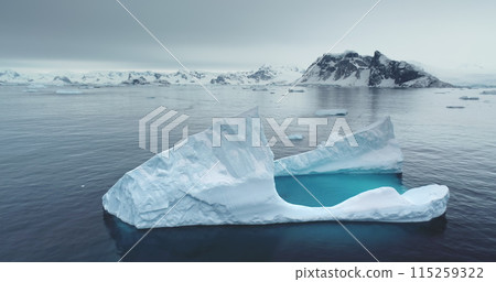 Arctic landscape with floating iceberg in tranquil blue waters. Snow-covered mountains in background. Melting glacier drift in Polar ocean. Ecology, melting ice, climate change, global warming concept 115259322