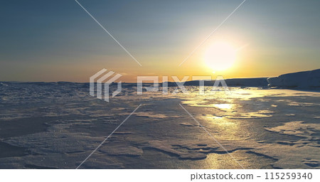 Fly over sunset frozen ocean in Antarctica. Sun warm glow reflect on icy surface. Antarctica travel background and exploration. Discover the beauty of South Pole. Desert white land of snow drone shot. Fly over sunset frozen ocean in Antarctica. Sun warm glow reflect on icy surface. Antarctica travel background and exploration. Discover the beauty of South Pole. Desert white land of snow drone shot. 115259340