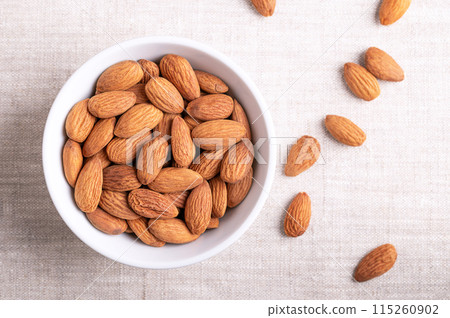 Almonds in a white bowl on linen fabric. Shelled, raw, whole and dried nuts, botanically drupes, seeds and fruits of Prunus dulcis. Ready-to-eat as a snack, or used as an ingredient for baking. Photo Almonds in a white bowl on linen fabric. Shelled, raw, whole and dried nuts, botanically drupes, seeds and fruits of Prunus dulcis. Ready-to-eat as a snack, or used as an ingredient for baking. Photo 115260902