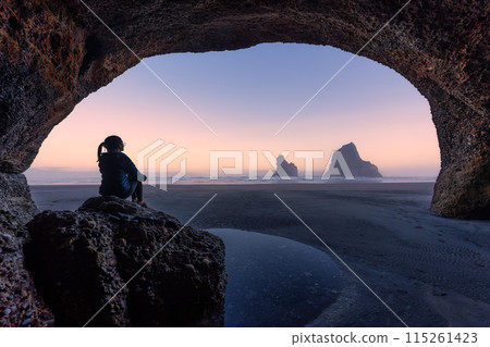 Female tourist sitting on rock in stone cave with Archway islands on Wharariki beach New Zealand 115261423