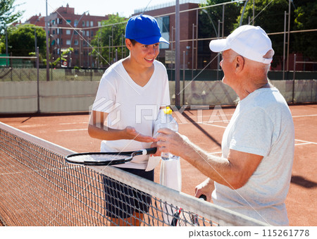 Grandfather and grandson talking on court playing tennis Grandfather and grandson talking on court playing tennis 115261778