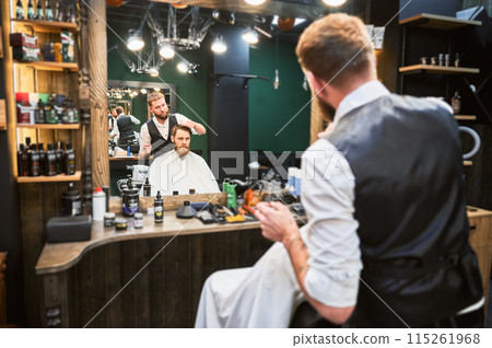 Hairdresser making final touches in new haircut. Comfortable atmosphere in modern barbershop. Hairdresser making final touches in new haircut. Comfortable atmosphere in modern barbershop. 115261968