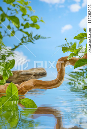 A dry tree branch in  brown color is bent, across a clear blue lake, behind is a sky and white clouds. Many different types of green plants grow on lakeside with many blank spaces in center 115262601