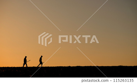 Two men farmers walk across the field, carrying work equipment 115263135