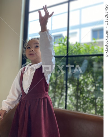 Asian little girl in a dress standing on chair Asian little girl in a dress standing on chair 115263450