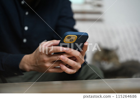 Young man sitting on couch reading text message and chatting in mobile application Young man sitting on couch reading text message and chatting in mobile application 115264686