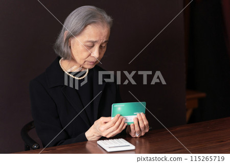 一位孤獨的老婦人穿著喪服看著她的銀行存摺 115265719