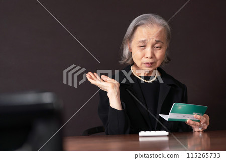 Senior woman in mourning clothes looking at bankbook - lonely Senior woman in mourning clothes looking at bankbook - lonely 115265733