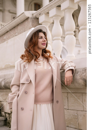 A woman in a hat stands on a set of stairs in front of a building. She is wearing a coat and a skirt. A woman in a hat stands on a set of stairs in front of a building. She is wearing a coat and a skirt. 115267565