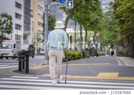 Back view of a senior woman using a walking stick to cross the street 115267680