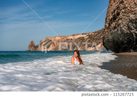Happy woman in bikini sits on the sea beach. Tanned girl sunbathing on a beautiful shore. Summer vacation or holiday travel concept 115267725
