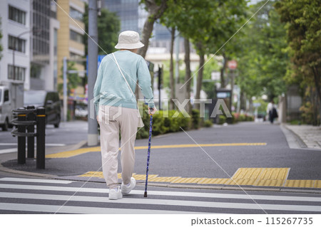 Back view of a senior woman using a walking stick to cross the street 115267735