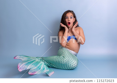 Shocked girl in mermaid costume sitting on blue background 115272023