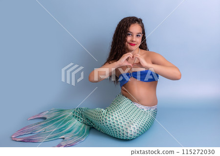 A pretty child girl in a mermaid costume, sitting on a blue background A pretty child girl in a mermaid costume, sitting on a blue background 115272030