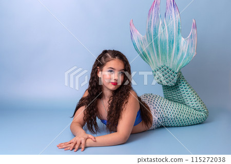 A pretty child girl in a mermaid costume lie isolated on light-blue background A pretty child girl in a mermaid costume lie isolated on light-blue background 115272038