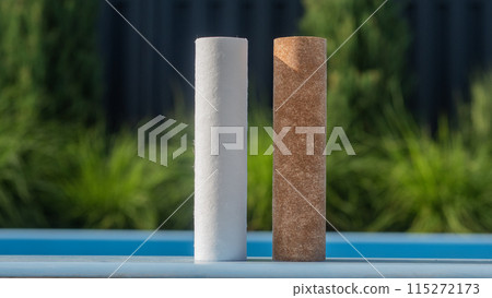 Two water filter cartridges, one clean and one dirty, standing outdoors. 115272173