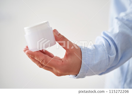 Hands in a blue shirt hold a jar of cream. Hands in a blue shirt hold a jar of cream. 115272206