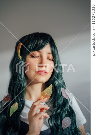 Beautiful tender woman with long dark green hair and multicolored skeleton leaves in ray of sunset light. Attractive fantasy girl, Young elven princess style. A gentle image. Autumn, fall concept. 115272336