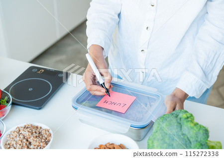 Healthy diet plan for weight loss, daily ready meal menu. Close up woman putting note on lunch box cooked in advance, ready to eat for lunch. Balanced portion with healthy dish. Pre-cooking concept. 115272338