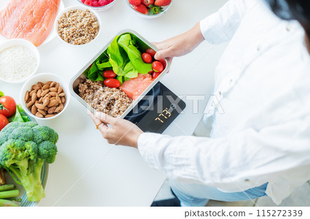 Healthy diet plan for weight loss, daily ready meal menu. Close up Woman weighing lunch box cooked in advance,ready to eat on kitchen scale. Balanced portion with healthy dish. Pre-cooking concept Healthy diet plan for weight loss, daily ready meal menu. Close up Woman weighing lunch box cooked in advance,ready to eat on kitchen scale. Balanced portion with healthy dish. Pre-cooking concept 115272339