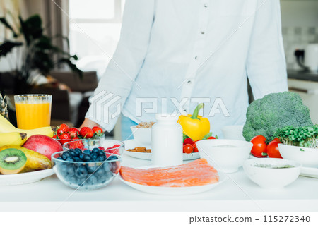 Selective Focus on white mockup jar with nutritional supplements and fresh food ingredients on kitchen table. Concept of Balanced Diet. Supplementing diet with missing vitamins. Dietary supplement 115272340