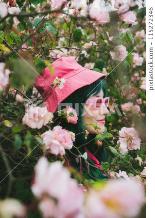 Summer portrait of young hipster woman with green hair in pink magenta bucket hat and sunglasses on blooming roses bush background. Urban street fashion. Gen Z. Summer vacation, fun, positive mood 115272346