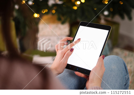 Mock-up, tablet in the hands of a woman. Christmas tree background. Concept of online shopping, discounts 115272551