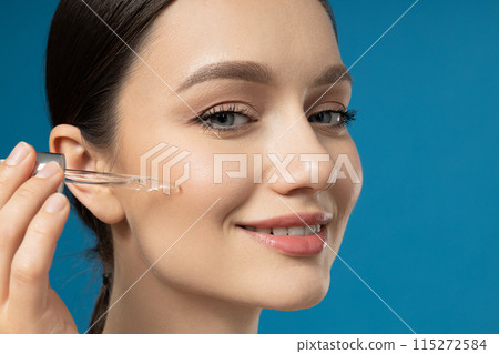 A brunette applies cosmetics with a dropper to her face 115272584